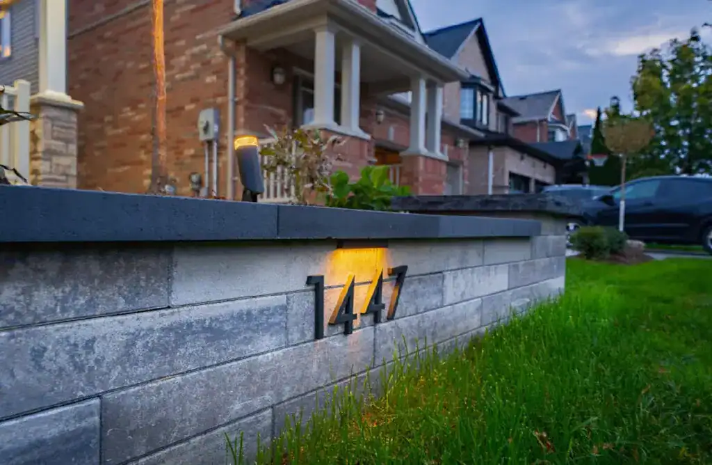 Landscape lighting and engraved house number on stone wall at residential home.