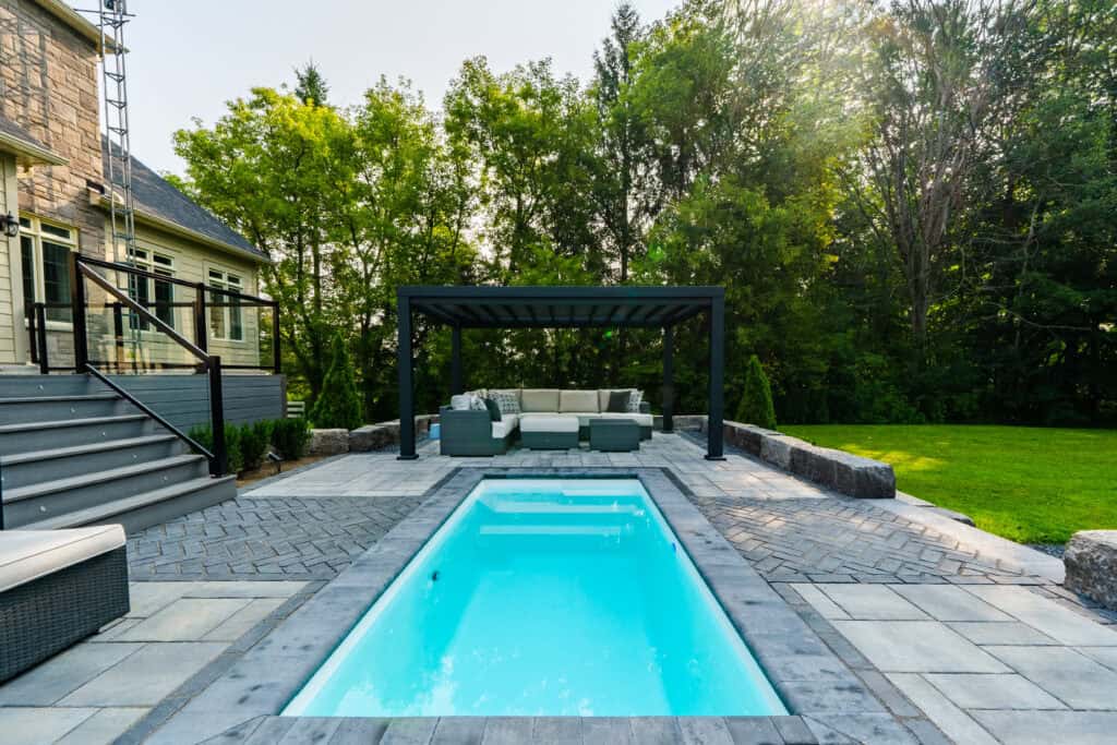 Stylish backyard with swimming pool, stone patio, and cozy lounge area under pergola.