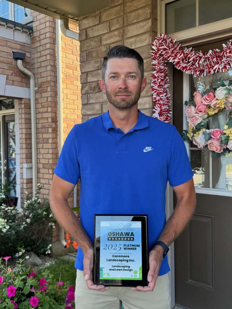 Landscape contractor holding award plaque outside house.