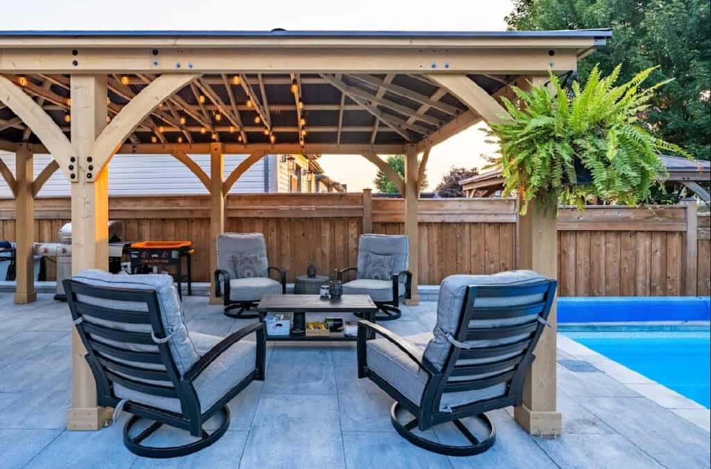 Modern backyard patio featuring a wooden pergola, cushioned chairs, and a private pool, ideal for landscaping and outdoor living.